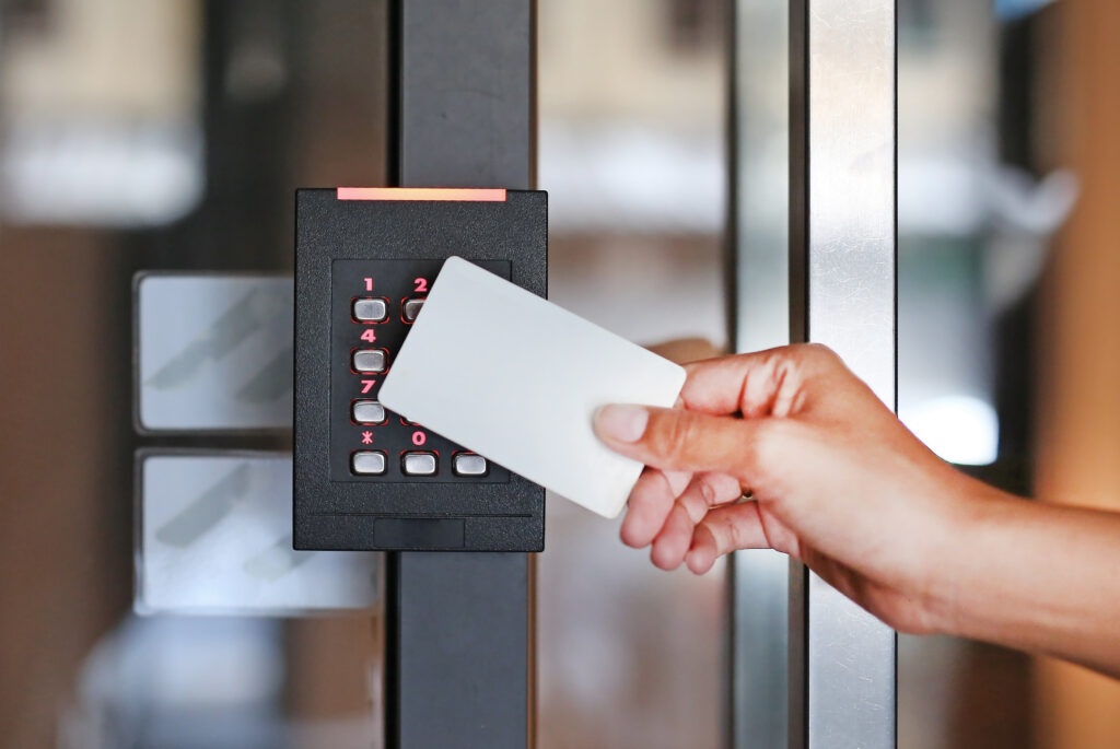 Person using keycard on modern electronic access control system mounted on glass door.