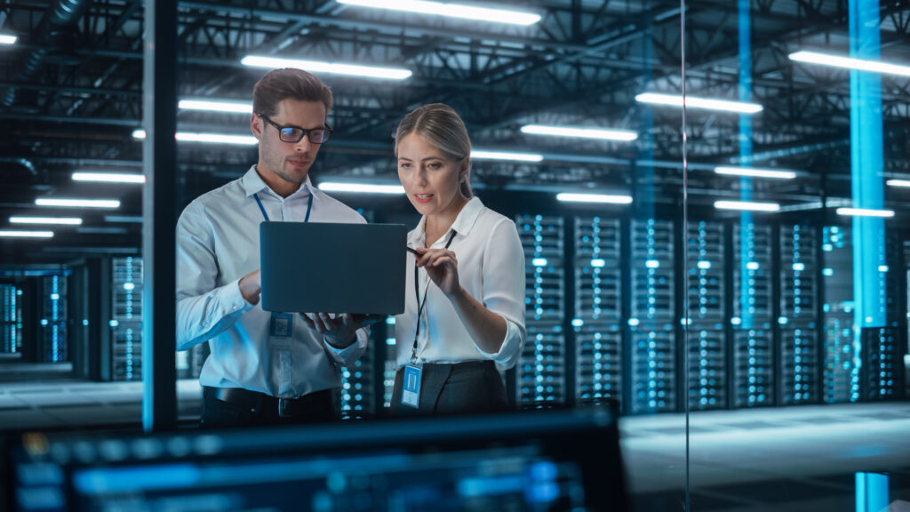 Two IT professionals collaborating with a laptop inside a modern data center for managed support planning